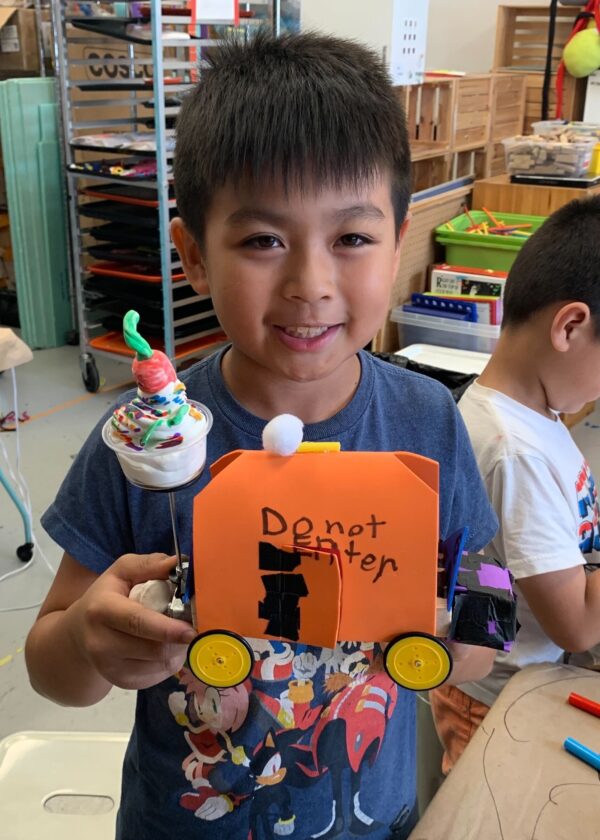 Photo of a child smiling at camera with a robot they built in front of them