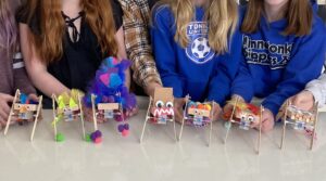 Photo of a bunch of robots lined up, held by the kids who built them