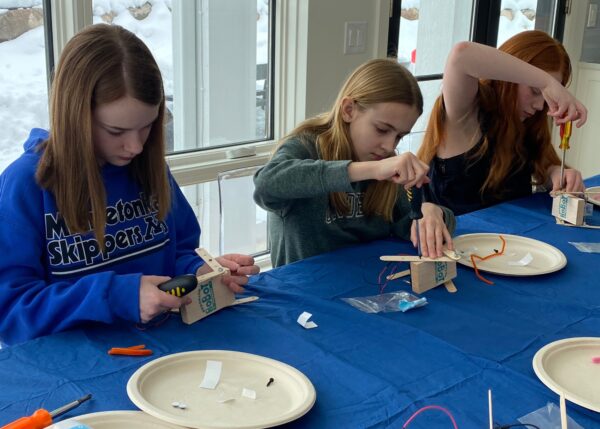 Photo of 3 students building their robots at blue table