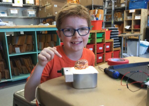 Photo of a child smiling at camera with a robot they built in front of them