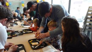 Group of children at a table with their parents/caregivers next to them, helping them build robots