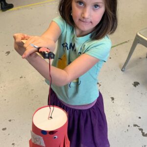 Photo of a child looking at camera holding a robot they built in front of them