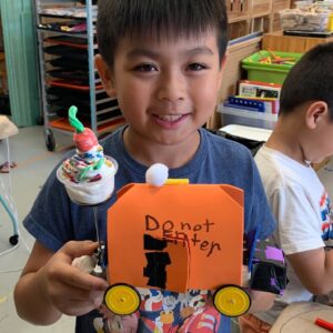 Photo of a child smiling at camera with a robot they built in front of them