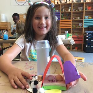 Photo of a child smiling at camera with a robot they built in front of them