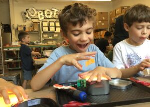 Photo of a child smiling with a lit-up robot they built in front of them