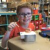 Photo of a child smiling at camera with a robot they built in front of them