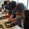 Group of children at a table with their parents/caregivers next to them, helping them build robots