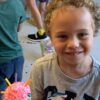 Photo of a child smiling at camera with a robot they built in front of them