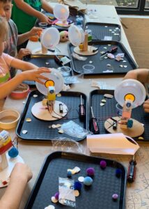 Photograph of a table covered with trays and kid-built robots in progress