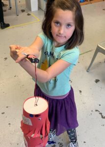 Photo of a child looking at camera holding a robot they built in front of them