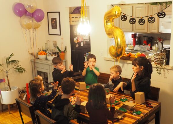 A photo of a birthday party in an apartment - all the kids are seated around the table with the teacher building robots