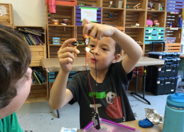 Photo of a child showing another child their lit-up LED circuit