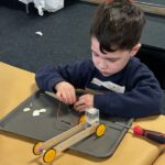 Young boy sitting and working on building a robot with wheels