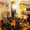 A photo of a birthday party in an apartment - all the kids are seated around the table with the teacher building robots