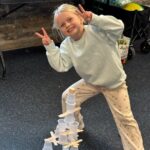 Young girl standing and showing the peace sign while standing over a stack of cups