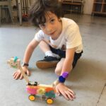 Photo of a child smiling at camera with a robot they built in front of them