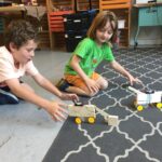 Photo of 2 kids sitting on the floor playing with their robots