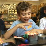 Photo of a child smiling with a lit-up robot they built in front of them