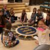 Group of students sitting in a circle on the floor, holding up the robots they built
