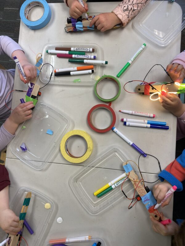 Overhead photo of kids decorating their robots with lots of markers and colorful tape in front of them