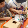 Close up on a robot project with two kids working on it