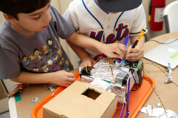 Close up on a robot project with two kids working on it