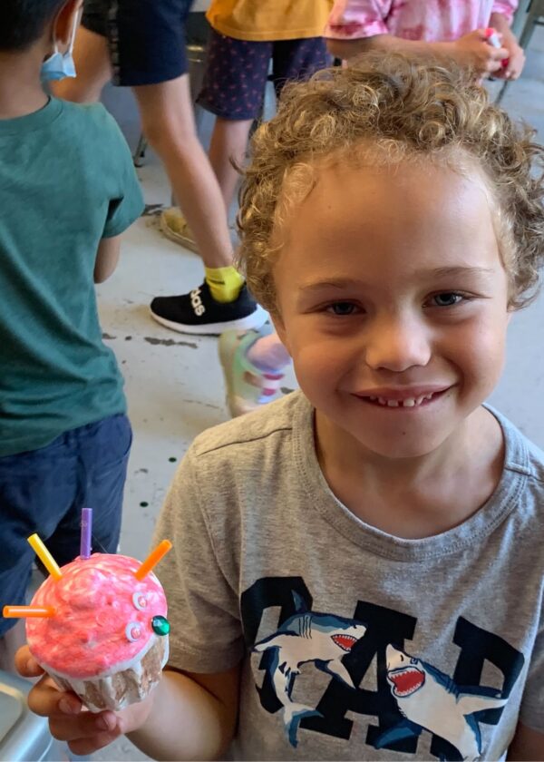 Photo of a child smiling at camera with a robot they built in front of them