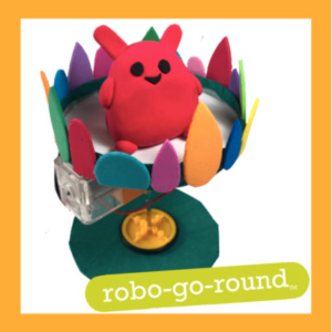 Picture of Robo-Go-Round robot with an orange square outline. The robot is a spinning cardboard platform with a Model Magic sculpture on top. The platform is decorated with different shapes and colors of foam paper attached to the edge. The sculpture is of a red little animal with black eyes and mouth. An green pill-shape has white lettering in it "robo-go-round TM".