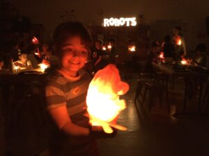 Photo of student holding up their illuminated robot in the dark