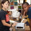 Two kids look to camera , taking a pause from working on a robot project together on the table