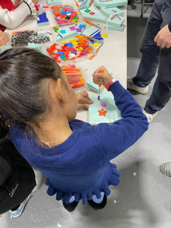 Photo over the shoulder of a child screwing a button onto a piece of foam.