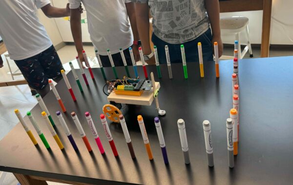 3 students stand near a table with a robot on it, surrounded by approximately 40 markers all standing up around it in a rectangle