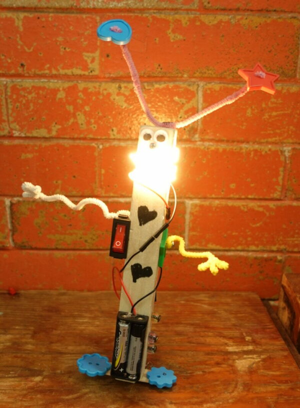 A whimsical robot with a glowing "face" sits on a table in front of a brick wall.