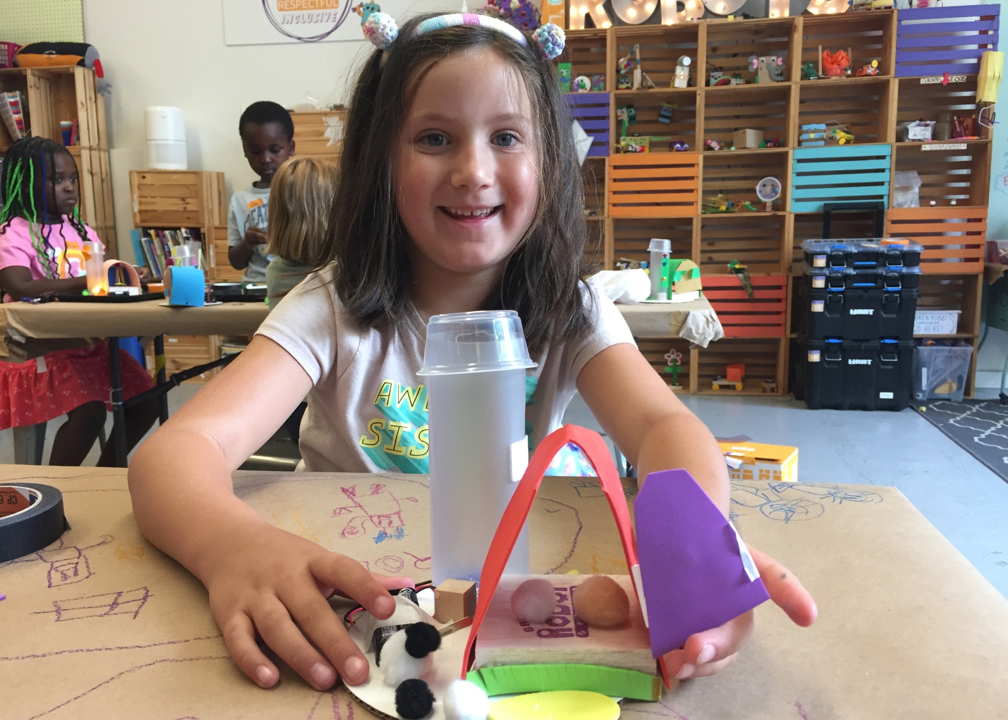 Photo of a child smiling at camera with a robot they built in front of them