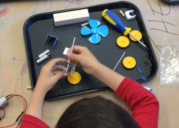 photograph of a tray of parts and a child's hands putting some together