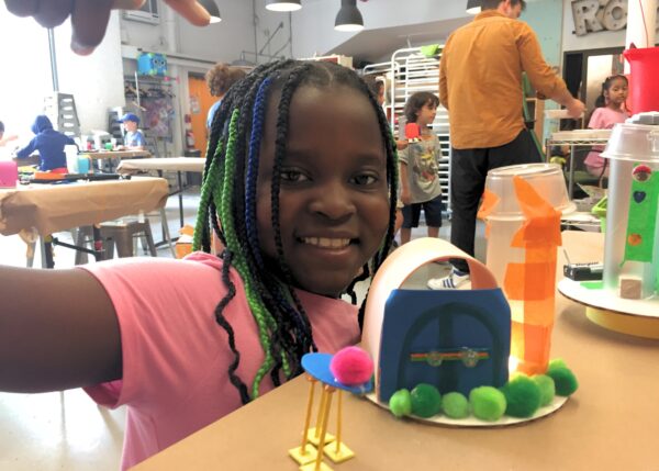 Photo of a child smiling at camera with a robot they built in front of them