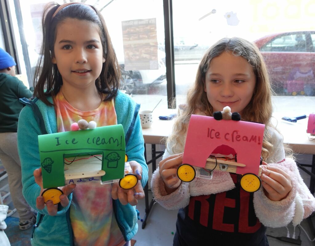 Two kids hold up their ice cream truck robots they made.