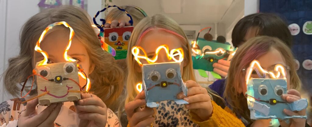 group of children holding up glowing robots they made in front of their faces